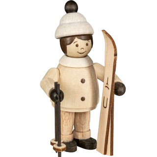 Die Abbildung zeigt eine Holzfigur einer Person, die in Winterkleidung gekleidet ist und einen Ski sowie einen Skistock hält. Die Figur trägt eine weiße Mütze mit einem schwarzen Bommel, einen weißen Mantel mit Knöpfen und schwarze Schuhe. 