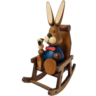 Der Osterhase in blau mit roter Fliege sitzt gemütlich im Schaukelstuhl und hält einen Vogel in der Hand_1
