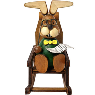 Der lustige grünfarbene Osterhase mit gelber Fliege und Brille sitzt gemütlich in einem Schaukelstuhl und liest Zeitung_2