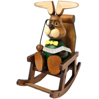 Der lustige grünfarbene Osterhase mit gelber Fliege und Brille sitzt gemütlich in einem Schaukelstuhl und liest Zeitung_1