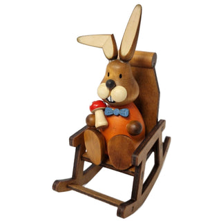 Der lustige, orange gekleidete Osterhase mit blauer Fliege sitzt gemütlich in einem Schaukelstuhl und hat einen Fliegenpilz in der Hand_1
