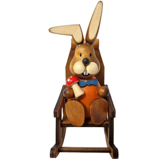 Der lustige, orange gekleidete Osterhase mit blauer Fliege sitzt gemütlich in einem Schaukelstuhl und hat einen Fliegenpilz in der Hand_2