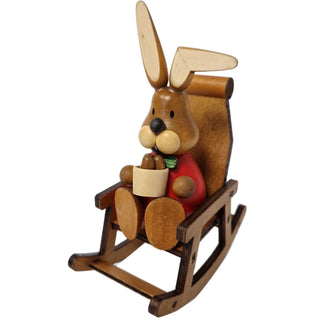 Der rot gekleidete Osterhase sitzt in einem Schaukelstuhl und hält ein Osterkörbchen mit Ostereiern in der Hand.