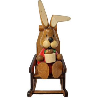 Der rot gekleidete Osterhase sitzt in einem Schaukelstuhl und hält ein Osterkörbchen mit Ostereiern in der Hand.