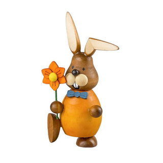 Orange gekleideter Osterhase mit einer Blume in der Hand