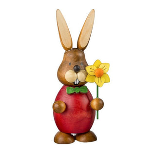 Rot gekleideter Osterhase mit einer gelben Narzisse in der Hand