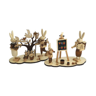 2 naturfarbeneSockel mit Osterhasen. Auf einem Sockel befindet sich eine kleine Hasenschule mit einer hasenlehrerin, einem Schulkind und einer Schultafel. Auf dem zweiten Sockel ist ein Osterhasenpaar mit einem Frühlingsbäumchen.