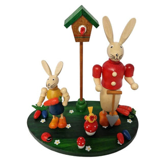 Farbige Osterhasen auf einem grünen Sockel im frühlingshaften Design und einem Vogelhaus