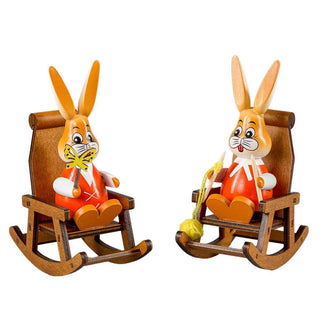 Farbiges Osterhasenpaar im Schaukelstuhl mit Schmettering und Strickzeug in der Hand