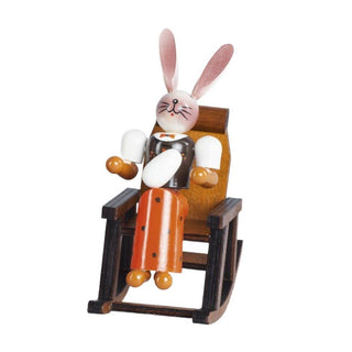 Farbige Osterhäsin im Schaukelstuhl aus Holz. Sie hält ein Osterei in der Hand.