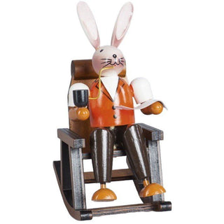 Farbiger Osterhase im Schaukelstuhl aus Holz. Der Hase liest gemütlich seine Zeitung un raucht eine Pfeife.