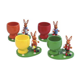 4 Eierbecher aud Holz in orange, rot, gelb und grün mit jeweils einem farbigen Osterhasen auf einem grünen Sockel mit Blumen und Ostereiern.