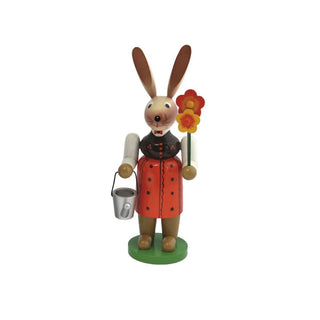Farbige Osterhäsin aus Holz mit Gießkanne und Blumen in der Hand.