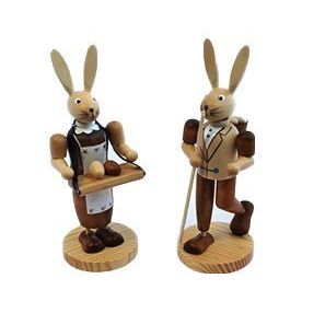 Naturfarbenes Osterhasenpaar. Der Osterhase hat einen Eierkorb auf dem Rücken und einen Wanderstab in der Hand. Die Häsin trägt einen Bauchladen mit Ostereiern
