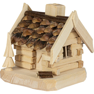 Kleine Holzmodell-Hütte mit Schindeldach und Schornstein auf einer unregelmäßig geformten Basis, daneben ein baumähnliches Element und ein Holzstück vor dem Eingang.