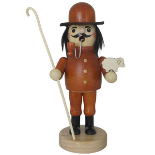 Ein hölzerner Räuchermann in der Rolle eines Schäfers steht auf einem runden Sockel. Er trägt einen orangefarbenen Mantel mit zwei Knöpfen, schwarze Stiefel und einen braunen Hut. Der bärtige Mann hält ein kleines weißes Schaf in der linken Hand und einen langen Hirtenstab in der rechten.