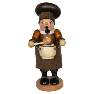 Das Bild zeigt ein Räuchermännchen namens „Dickbauch Koch“, das 26 cm groß ist. Es handelt sich um eine Holzfigur, die als Koch gestaltet ist. Die Figur trägt eine braune Kochmütze und Schürze, hält einen Holzlöffel in der rechten Hand und einen Kochtopf in der linken Hand. Der Körper des Räuchermännchens ist rundlich und es steht auf einem runden Holzsockel.