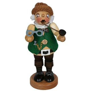 Holzfigur eines dickbäuchigen Opas mit grünem Filzmantel, braunen Stiefeln und Mütze. Die Figur hält eine Pfeife in der rechten Hand und eine Brille in der linken Hand. Sie steht auf einem runden Holzsockel.
