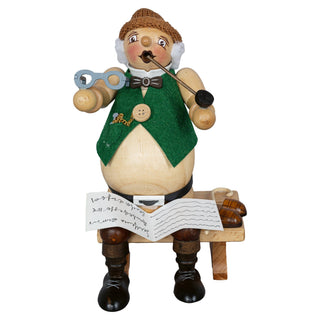 Das Bild zeigt ein handgefertigtes Räuchermännchen namens 'Dickbauch Opa', das 23 cm groß ist und auf einer Bank sitzt. Das Männchen trägt eine grüne Weste mit einem goldenen Kettendetail, eine Fliege und hält eine Pfeife in der rechten Hand. Vor ihm liegt ein Buch mit handgeschriebenem Text.