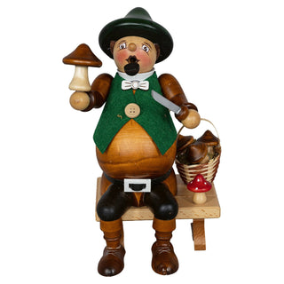 Holzfigur eines sitzenden Räuchermännchens mit dickem Bauch, grünem Hut und Weste. In der rechten Hand hält es einen Pilz, in der linken Hand ein Messer. Neben ihm steht ein Korb voller Pilze.