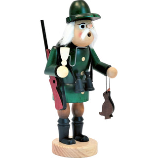 Holzfigur eines Jägers mit grünem Hut und Mantel, der ein Fernglas um den Hals trägt, in der linken Hand erlegte Gänse hält und in der rechten Hand eine Pfeife.