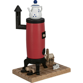 Räucherofen in Form eines roten Küchenherds mit schwarzem Schornstein, weißem Teekessel auf der Oberseite und kleinen dekorativen Elementen wie einem Korb, Hausschuhe und einer Katze auf einer Holzplatte..