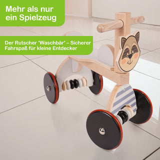 Ein hölzernes Kinder-Rutschfahrzeug in Form eines Waschbären mit vier Rädern, zwei Griffen zum Festhalten und einer Sitzfläche. Auf der Vorderseite ist ein lächelndes Waschbärgesicht zu sehen. Der Boden ist gefliest und reflektiert das Fahrzeug leicht. Im Bild steht der Text: „Mehr als nur ein Spielzeug – Der Rutscher 'Waschbär' – Sicherer Fahrspaß für kleine Entdecker“.