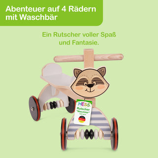 Ein hölzernes Kinderfahrzeug mit dem Namen „HESS Rutscher Waschbär“. Der Text auf dem Bild lautet: „Abenteuer auf 4 Rädern mit Waschbär – Ein Rutscher voller Spaß und Fantasie“.