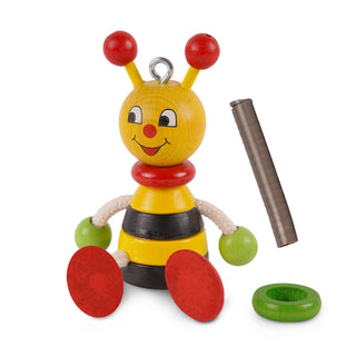 Ein buntes Holzspielzeug in Form einer Biene mit gelbem Kopf, roten Fühlern, schwarzen und weißen Augen, roter Nase und lächelndem Mund. Der Körper ist gelb-schwarz gestreift mit grünen runden Händen und roten runden Füßen. Neben dem Spielzeug liegen ein metallisches Spiralelement und zwei grüne Ringe.