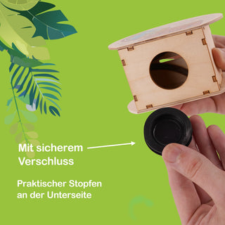 Zylindrische Spardose aus Holz mit einem runden Loch an der Seite zum Einwerfen von Münzen. Die Unterseite ist mit einem schwarzen Stopfen verschlossen. Der Hintergrund ist grün und mit Blättern verziert. Auf dem Bild steht: „Mit sicherem Verschluss“ und „Praktischer Stopfen an der Unterseite“.