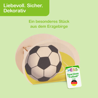 Runde Spardose aus hellem Holz mit einem schwarz-weißen Fußballmotiv auf gelbem Hintergrund. Oben befindet sich ein Schlitz zum Einwerfen von Münzen. Links im Bild steht in weißer Schrift auf grünem Hintergrund: „Liebevoll. Sicher. Dekorativ“. Darunter in grüner Schrift: „Ein besonderes Stück aus dem Erzgebirge“. Rechts unten ist ein Etikett mit der Aufschrift: „HESS Spardose 'Fußball' farbig 100% MADE IN GERMANY“.