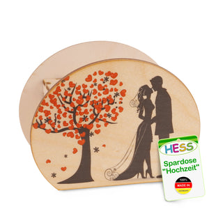  Ovale Spardose aus Holz mit einem romantischen Motiv auf der Vorderseite: Ein Baum mit roten herzförmigen Blättern und ein Brautpaar in schwarzer Silhouette, das sich gegenübersteht. Die Braut trägt einen Schleier. Rechts unten befindet sich ein Etikett mit der Aufschrift: „HESS Spardose 'Hochzeit' 100% MADE IN GERMANY“.