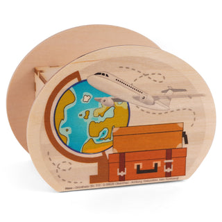 Spardose aus Holz mit der Aufschrift „Reisekasse“. Auf der Vorderseite sind ein teilweise sichtbarer Globus mit blauen Ozeanen und grünen Landmassen, ein darüber fliegendes Flugzeug mit gestrichelter Flugbahn sowie ein orangefarbener Koffer mit braunen Gurten und silbernen Schnallen abgebildet. Unten steht in kleiner Schrift: „Hess – Grünthaler Str. 112 – D 09628 Olbernhau – Achtung: Dekoration, kein Spielzeug!“.