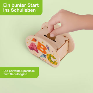 Bunte Spardose aus Holz mit farbenfrohen Buchstaben A, B und C sowie kleinen Schultüten als Dekor. Die Gestaltung vermittelt einen fröhlichen Start ins Schulleben. Der Text auf dem Bild lautet: ‚Ein bunter Start ins Schulleben – Die perfekte Spardose zum Schulbeginn‘.