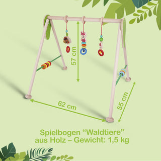 Ein hölzerner Spielbogen namens „Waldtiere“ mit einer Breite von 62 cm, Höhe von 57 cm und Tiefe von 55 cm. An der oberen Querstrebe hängen bunte Spielzeuge: ein rosa Fuchs, ein grüner Frosch und mehrere Ringe. Der Spielbogen wiegt 1,5 kg.