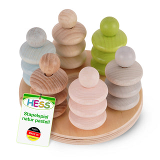 Ein rundes Holzspielzeug namens „Stapelspiel natur pastell“ der Marke HESS. Es besteht aus sechs stapelbaren Figuren in Pastellfarben: blau, grün, grau, rosa und natur. Jede Figur hat eine runde Basis und mehrere runde Holzscheiben, die übereinander gestapelt sind. Das Spielzeug steht auf einer runden Holzplatte. An einer Figur ist ein Etikett befestigt mit dem Text: „HESS Stapelspiel natur pastell 100% MADE IN GERMANY“.