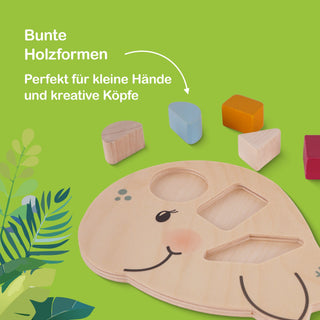 Holzspielzeug auf grünem Hintergrund mit einer flachen, holzfarbenen Basis in Form eines lächelnden Tieres. Die Basis enthält drei Aussparungen: Kreis, Dreieck und Rechteck. Daneben liegen fünf bunte Holzformen: rotes Rechteck, gelbes Quadrat, blaues Oval, naturfarbenes Halboval und naturfarbenes Dreieck. Links unten sind grüne Blätter zu sehen. Oben links steht: ‚Bunte Holzformen – Perfekt für kleine Hände und kreative Köpfe‘.
