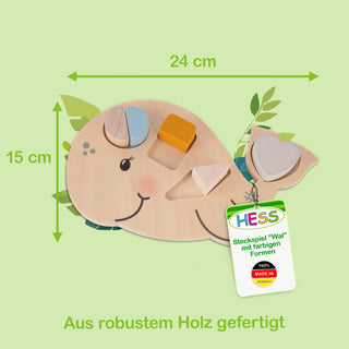 Steckspiel in Form eines Wals aus robustem Holz. Der Wal enthält farbige Formen, die in passende Aussparungen gesteckt werden können. Die Maße des Spiels betragen 24 cm Breite und 15 cm Höhe. Ein Etikett trägt die Aufschrift: ‚HESS Steckspiel ‚Wal‘ mit farbigen Formen – 100% Made in Germany‘.