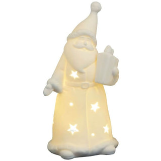 Eine weiße Weihnachtsmannfigur aus Porzellan ist von innen beleuchtet. Licht scheint durch sternförmige Aussparungen im Mantel und verleiht der Figur ein warmes Leuchten. Der Weihnachtsmann hält ein Geschenk in einer Hand.