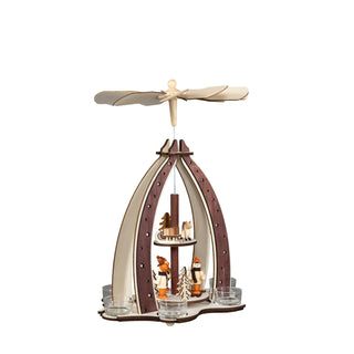 Ein Weihnachtspyramiden-Dekorationsstück aus Holz mit einem drehbaren Flügelrad oben, das durch die Wärme von Teelichten angetrieben wird. Die Pyramide zeigt Winterkinder, Reh, Schlitten und Bäumen auf zwei Ebenen, umgeben von sternverzierten Bögen. Ansicht von links.