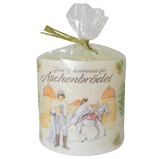 Ein Windlicht aus Wachs mit einem Durchmesser von 10 cm. Auf dem Windlicht ist eine Szene aus dem Märchen „Drei Haselnüsse für Aschenbrödel®“ abgebildet: Der Prinz in mittelalterlicher Kleidung blickt auf eine Prinzessin, die auf einem weißen Pferd sitzt. Im Hintergrund ist das Schloß zu sehen. Oben auf dem Windlicht steht in geschwungener Schrift „Drei Haselnüsse für Aschenbrödel“. In Geschenkverpackung