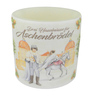 Ein Windlicht aus Wachs mit einem Durchmesser von 10 cm. Auf dem Windlicht ist eine Szene aus dem Märchen „Drei Haselnüsse für Aschenbrödel®“ abgebildet: Der Prinz in mittelalterlicher Kleidung blickt auf eine Prinzessin, die auf einem weißen Pferd sitzt. Im Hintergrund ist das Schloß zu sehen. Oben auf dem Windlicht steht in geschwungener Schrift „Drei Haselnüsse für Aschenbrödel“.