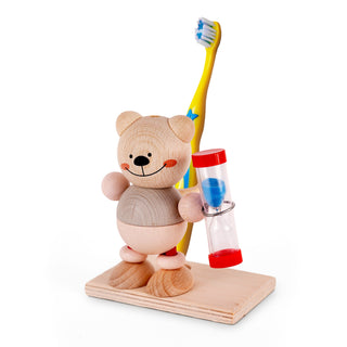 Ein hölzerner Bär steht auf einer rechteckigen Holzplatte. In der linken Hand hält er eine Sanduhr mit blauem Sand. Auf seinem Rücken befindet sich ein gelber Zahnbürstenhalter mit einer Zahnbürste darin. Die Zahnbürste ist gelb mit blauen Sternen und hat weiße Borsten mit blauen Spitzen.