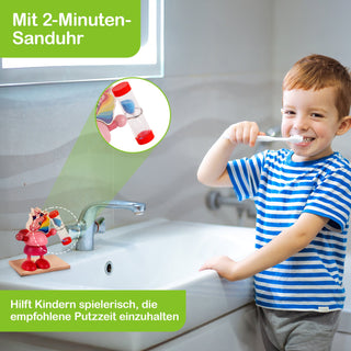 Ein Kind mit blau-weiß gestreiftem T-Shirt steht in einem Badezimmer vor einem Waschbecken und putzt sich die Zähne. Auf dem Rand des Waschbeckens steht eine Sanduhr mit roten Enden, die von einer kleinen Spielzeugfigur gehalten wird und als 2-Minuten-Timer dient. Text im Bild: „Mit 2-Minuten-Sanduhr“ und „Hilft Kindern spielerisch, die empfohlene Putzzeit einzuhalten“.