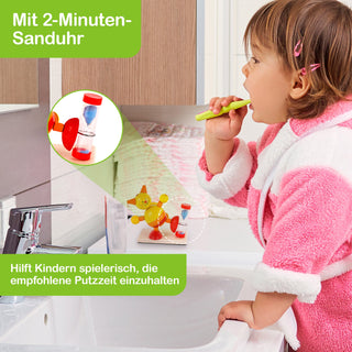 Ein Kind in einem rosa-weißen Bademantel steht vor einem Waschbecken und putzt sich die Zähne. Links oben im Bild ist ein grünes Feld mit dem Text „Mit 2-Minuten-Sanduhr“. Darunter ist eine vergrößerte Ansicht einer rot-blauen Sanduhr zu sehen. Unten links steht in einem weiteren grünen Feld: „Hilft Kindern spielerisch, die empfohlene Putzzeit einzuhalten“.