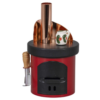 Kleiner Räucherofen in Form eines roten Küchenherds mit schwarzer Oberseite und Tür, kupferfarbenem Schornstein. Ein kleiner Keramikkrug mit grünem Blattmuster und roten Punkten steht auf der Herdplatte. An der Herseite hängt Holzgriff-Werkzeug.