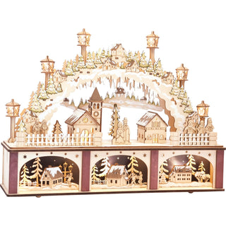 LED Lichterbogen Stadt mit beleuchtetem Sockel. Im oberen Teil des Lichterbogens spielt sich die klassische Stadtszene ab. Winterlich gekleidete Spaziergänger aus Sperrholz gehen zur festlich beleuchteten Kirche. Im unteren Teil werden drei Mini-Geschichten erzählt. In jeden Segment befindet sich ein verschneites Haus, wahrscheinlich am Stadtrand. Besonders detailreich wurde der Bogen aus verschneiten Tannen und beleuchten Laternen, die alles überspannen, gestaltet.