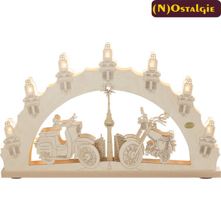 Der 7-flammige Schwibbogen „Moped“ mit 3D Effekt, zeigt die legendären Modelle Simson und Schwalbe aus DDR-Zeiten. In der Mitte des Schwibbogens zeichnet sich sanft eine Straße ab. Diese führt zum Berliner Fernsehturm. Die Umrandung mit den 7 Zündkerzen greift das Thema voll und ganz auf. Unter Beleuchtung wirkt der Bogen besonders schön.