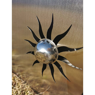 Nahaufnahme eines Sonnensymbols aus Edelstahl mit glänzender, halbkugeliger Mitte und ausgeschnittenen Strahlen, integriert in eine Edelstahl‑Gartensäule, metallisch schimmernde Oberfläche mit Spiegelreflexionen.