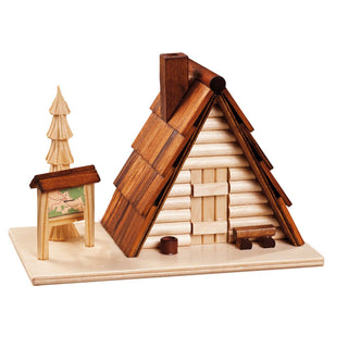 Diese kleine Skihütte als Räucherhütte ist mit viel Liebe zum Detail verarbeitet worden. Das Dach ist aus kleinen Holzstreifen. Auch das geschnitzte Bäumchen, die kleine Bank und ein Wegweiser verfeinern das Motiv. Eine aktive Räucherkerze stellt man in das Häuschen, damit wird der Weihnachtsduft aktiviert.